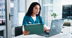 A healthcare worker using a computer and tablet at a clinic